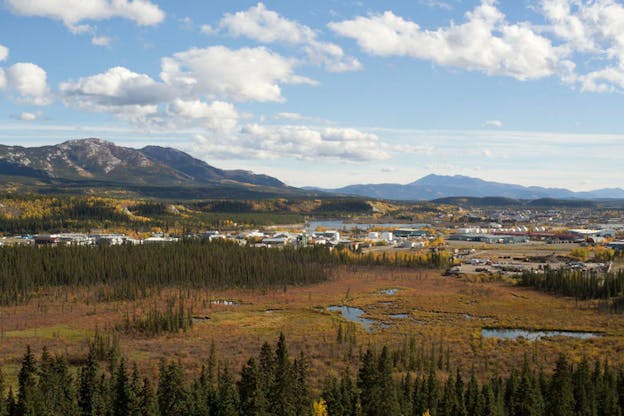 White clouds cast shadows over a marsh and rural valley town in autumn. In the distance, mountains stretch across the horizon turning blue.