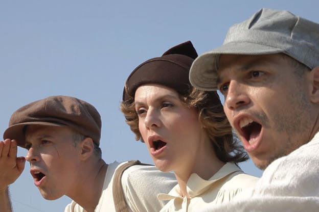 Close-up of three persons wearing newsboy caps and looking at something out-of-frame with their mouths open expressively.