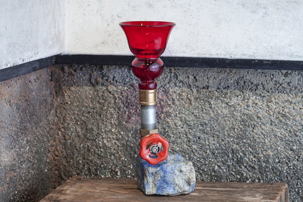 A blue and gray rock situated on a bench supports a metallic tube leading to a red class cup.