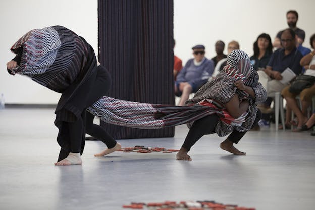 Two performers surround their bodies and heads with the same multipatterned cloth as they push away from each other.
