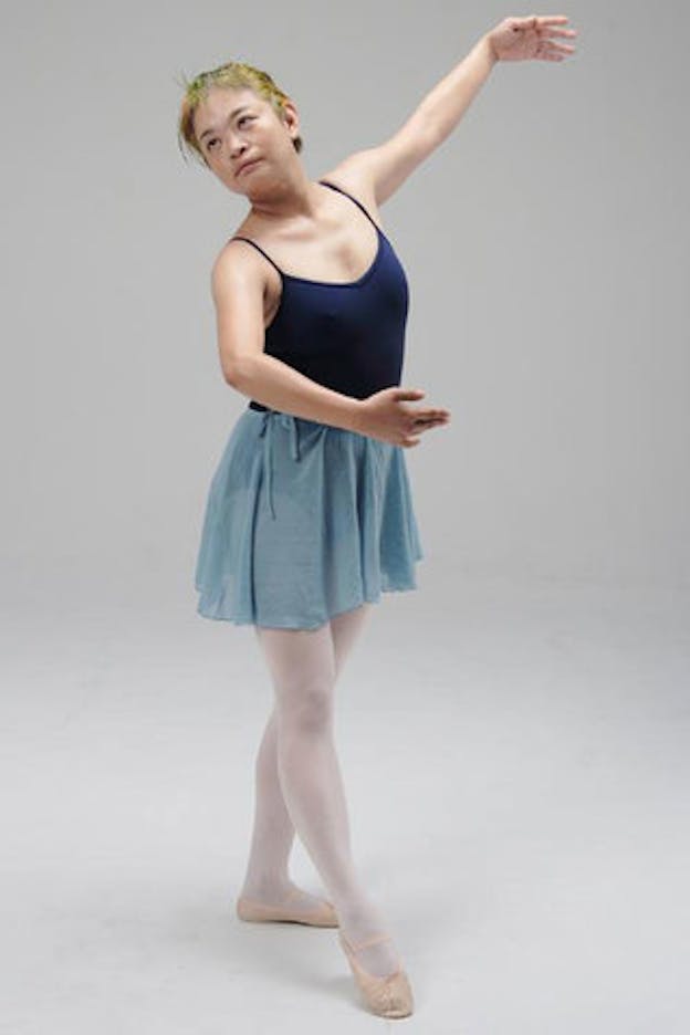Nexus6 performs in a bare white space. She wears a blue leotard, blue tulle skirt, and pink ballet shoes. She is in third position. 
