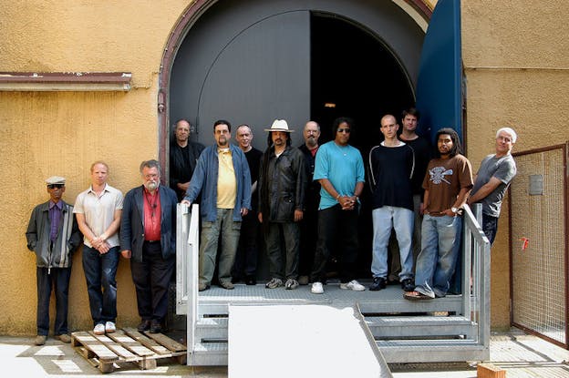 A group of people stand next to each other in front of an entrance with three steps.