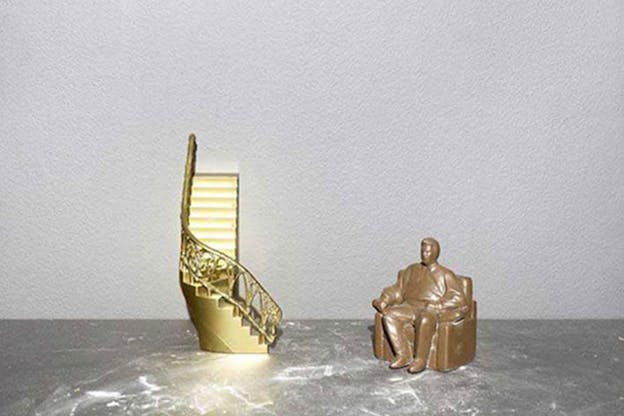 Close-up of a miniature gold winding staircase and a bronze seated man. 