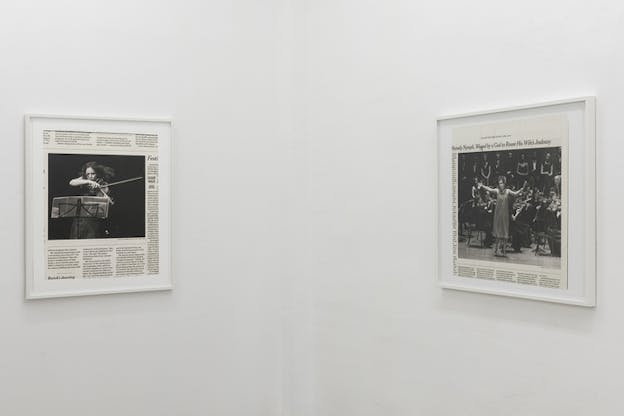 Two frames with cut outs from newspapers showcasing a person playing a violin and an orchestra stand on side by side walls.