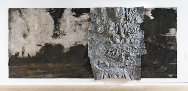 A long rectangular multimedia painting with black ink, soil, and patches that remain off-white. Three sheets of crinkled metallic grey material are attached in a vertical line towards the right of the painting. 