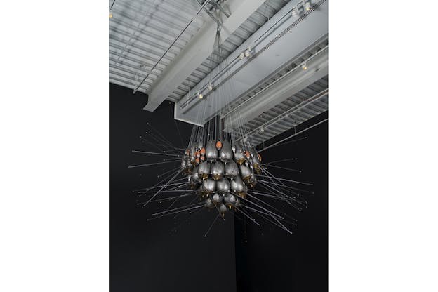 A structure containing silver and orange metallic ovals with antennae stuck on them hangs from the ceiling through multiple strings.