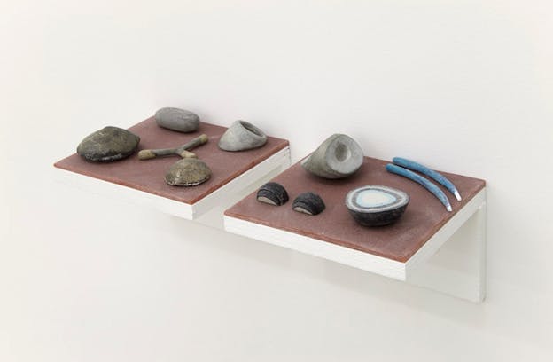Right-side view of white and brown painted wooden shelves supporting objects shaped like a forked twig, geods, rocks, and blue painted sticks.