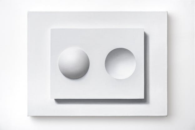 An oil painting painted in greyscale depicting a white rectangle hovering above the surface of the canvas with small concave dome emerging out of the surface on the left side and the inverse, or a convex dome impressed into the space, next to it. 