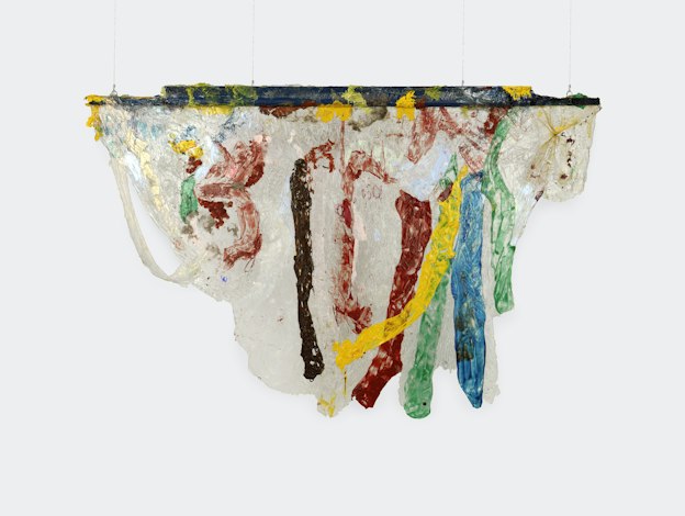 A hanging sculpture of primarily opaque white acrylic draped over a thin plank of wood that is painted dark blue. Areas of green, blue, yellow, red, and brown paint run vertically along the draped white acrylic, resembling drips. Areas of red and yellow appear along the top of the piece. The bottom edges of the draped acrylic are smooth and sloping. 