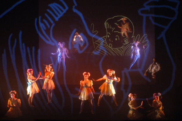Figures on a stage are illuminated by projections of blue and yellow lines creating a cartoonish image of children.