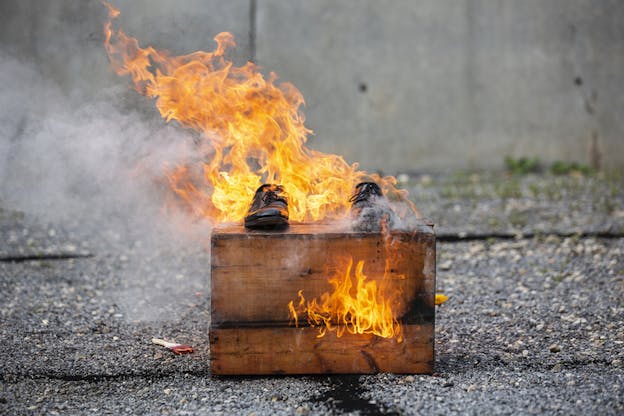 Two black dress shoes sit on top of a wooden box engulfed in flames.