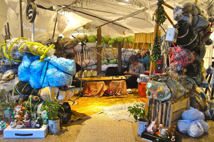 Beglarian and a fellow performer in a warmly-lit hut built of repurposed trash bags. 