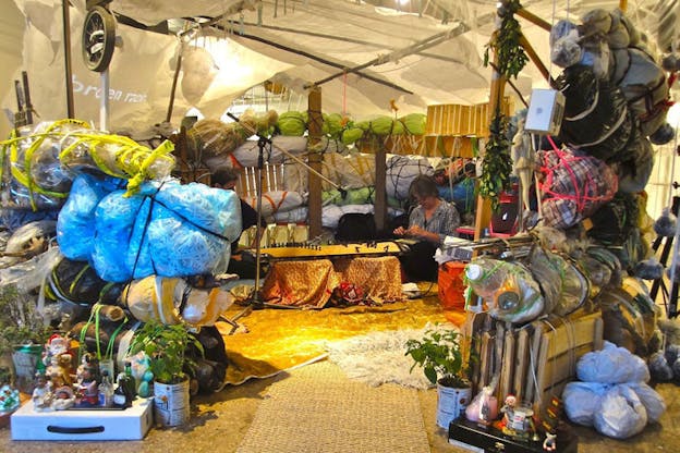 Beglarian and a fellow performer in a warmly-lit hut built of repurposed trash bags. 