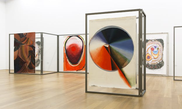 Abstract paintings supported by wide glass frames. Colors of red, blue and green dominate the theme. 