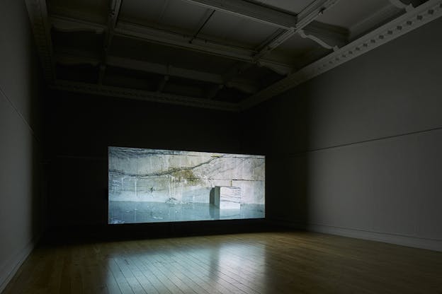 A projection on a black wall shows a cubed black marbled rock against a rock wall.