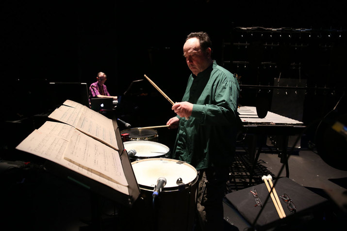 Winant holds a drum stick and looks at sheet music while playing onstage.