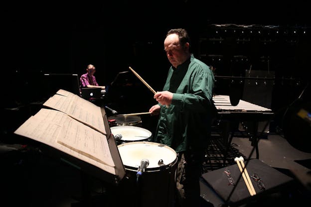 Winant holds a drum stick and looks at sheet music while playing onstage.