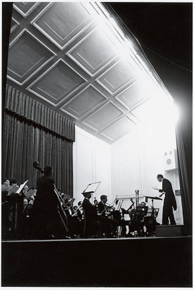 A black and white performance still with Brown in front of an orchestra in a room with high ceilings. 