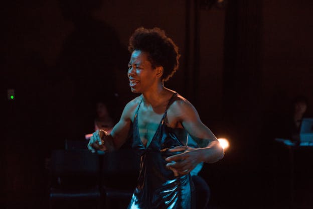 A person dressed in metallic silver performs while lights shine on them.