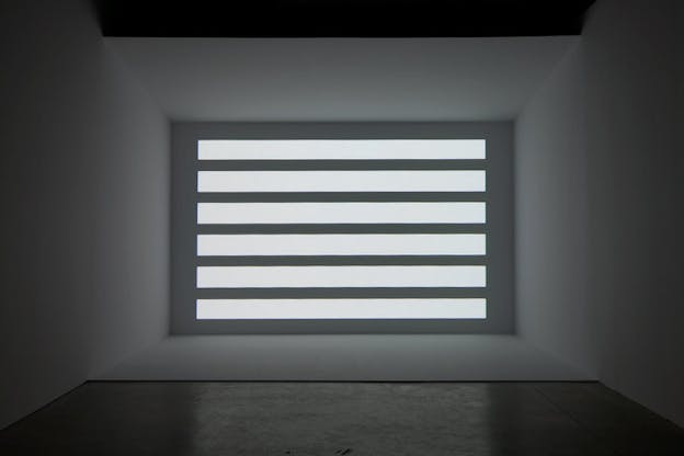 At the far wall of a dark grey room, there is a grey wall with various horizontal bars of light projected onto it.