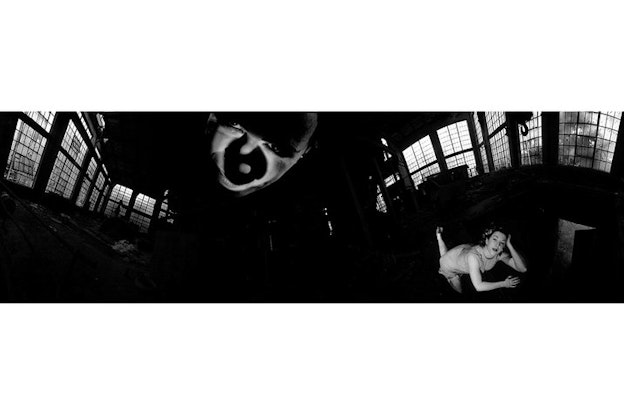 A black and white panoramic image has in the center of it closest to the viewer a face half covered by shadows. Behind it another figure lies on the floor their angled hand supporting their head. 