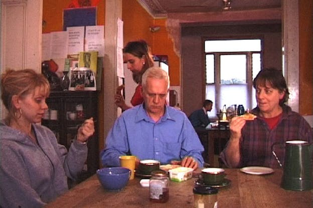 Photograph of three people in a dining place, sitting at a table. Cups of coffee, bowls and jam jars sit in front of them.