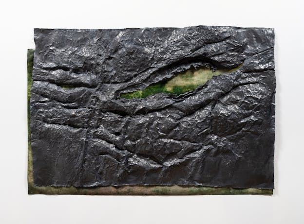 A rectangular painting laid underneath a sheet of dark grey geological material with one horizontal slash near the center. The top layer is offset from the bottom layer, the left and bottom edges of the painting are visible beneath the top layer and through the slash. in the painting. Shades of brown and green meld into one another. 