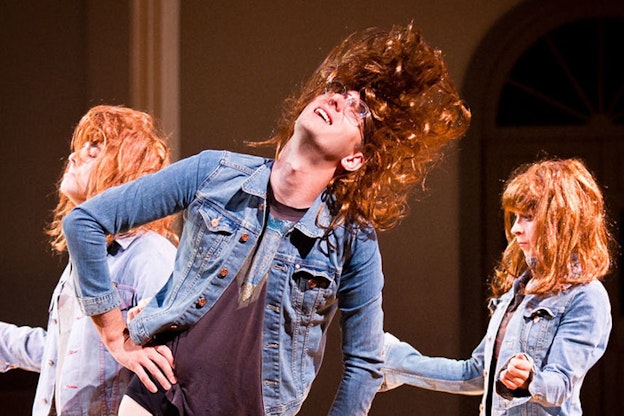 Two people wearing blonde wigs and jean jacket stand sideways with their hands on either side. In the front closest to the viewer a third person flips their long brown hair backwards as they rest one arm on the hip.