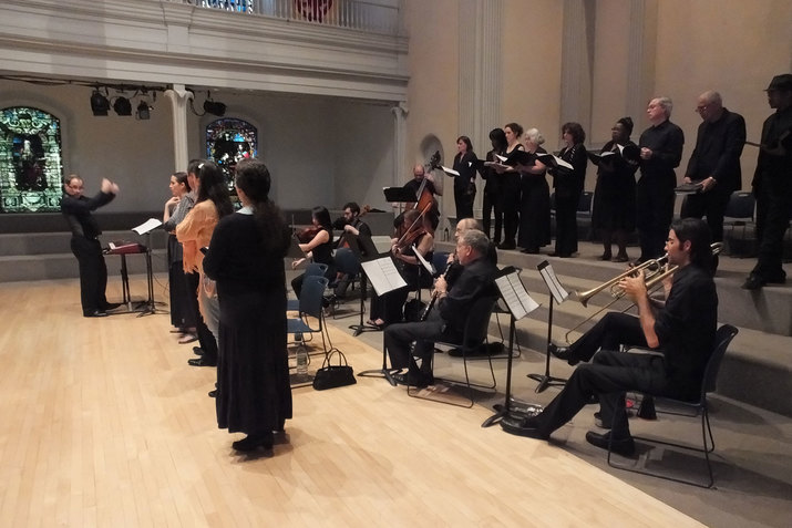 Side-angle shot of a conductor leading an ensemble and choir in a day-lit church setting. 