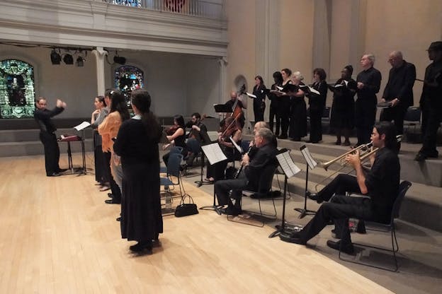 Side-angle shot of a conductor leading an ensemble and choir in a day-lit church setting. 