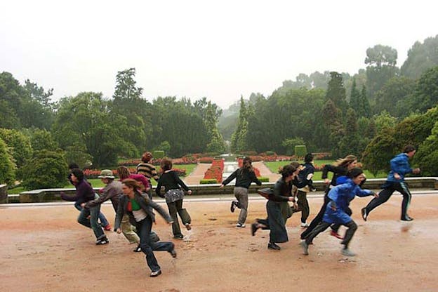 Photograph of a group of people split in the middle and running on opposite directions. Behind them in the background are full trees with a small rose garden.  