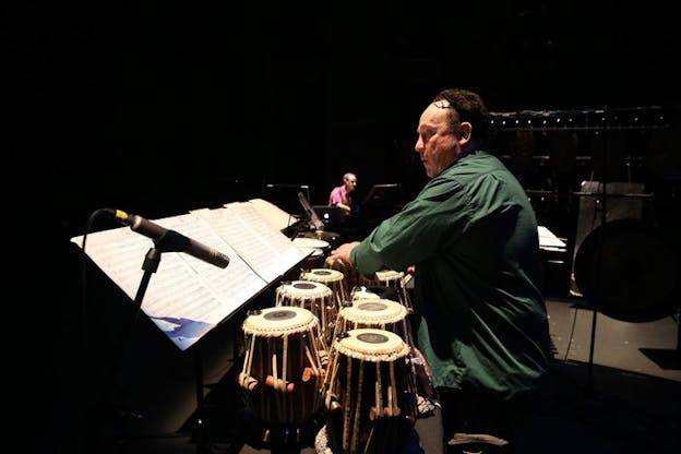 Winant reads sheet music on stage while playing an arrangement of leather hand drums.