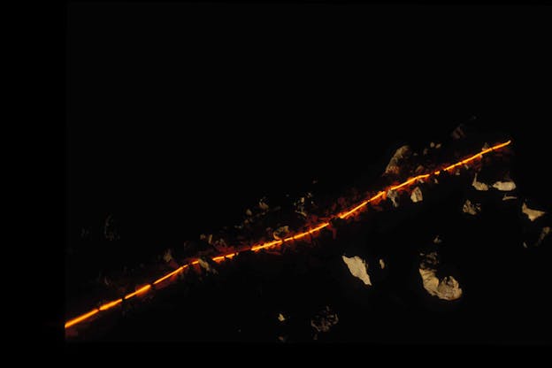 A darkly lit image with one thin line of orange light on the ground which illuminated a few rocks around it.