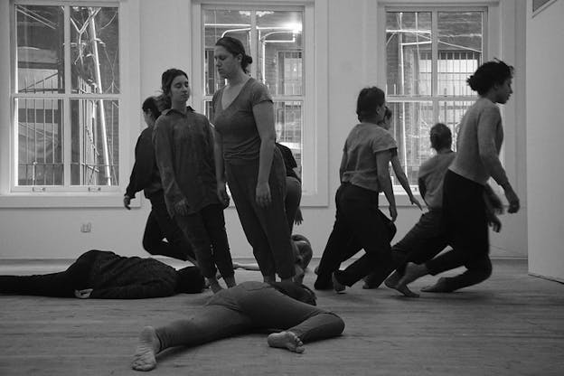 Black and white photograph of performers with their eyes closed facing in different directions and leaning forward or sideways, two of them lay on the ground.