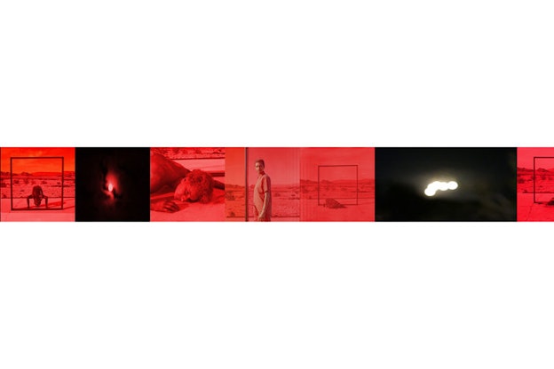 Collage of images resembling a red-hued film roll depict a person standing behind a large frame erected against a desert backdrop, a close-up of a person's face resting against concrete, and blurred white orbs evoking the sun and moon against a red and black sky.