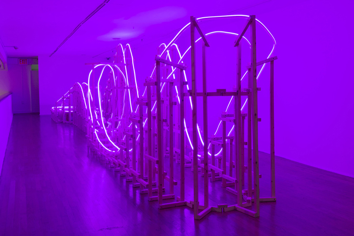 A wooden structure similar to a fun park's train rails is lighted by purple neon lights on its outline.
