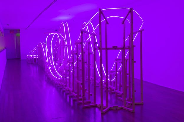 A wooden structure similar to a fun park's train rails is lighted by purple neon lights on its outline.