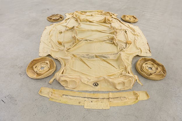 Yellow material cut out resembling a car is laid on the floor, four yellow deflated tires on each side.  