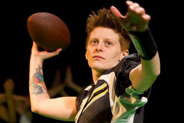 A person dressed in football player clothing holding a football behind their head in the motion of throwing it.