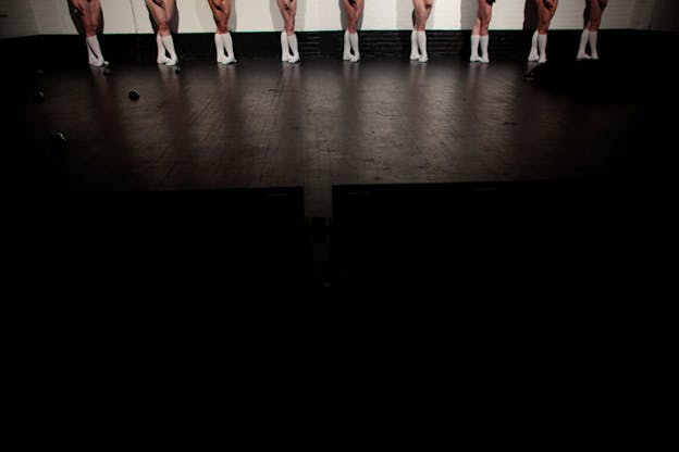 Wide angle shot of nine dancers' legs in fifth position, all aligned and wearing identical knee-high socks.
