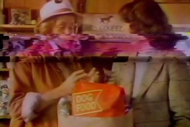 Blurry warm-toned and grainy image of two women facing each other at a grocery store beside a sack with an orange bag labeled 