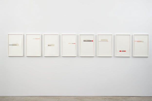 Eight framed paintings with white backgrounds and lines of blue, beige and red aligned on a wall.