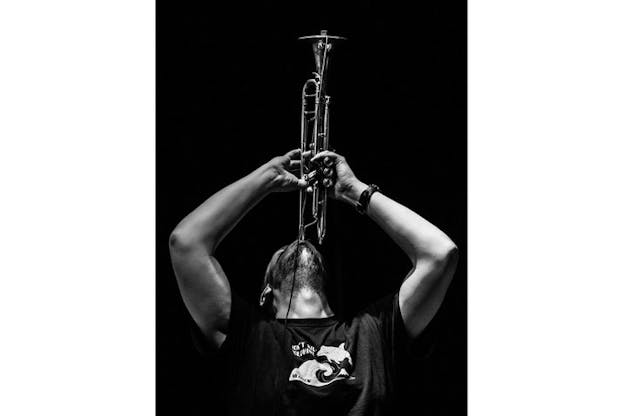 Black and white photograph of Wooley tilting his head back and raising his arms, playing the trumpet directly above his head. 