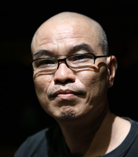Portrait of Ngoc Dai dressed in a black shirt and black framed square glasses.