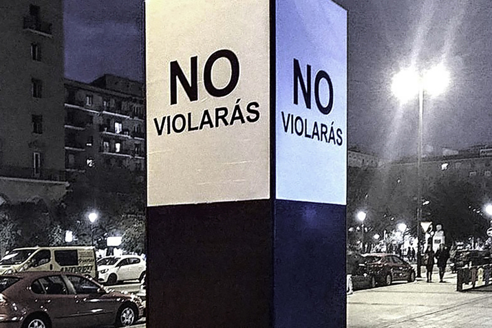 A thick pole in a street surrounded on each side by white posters with the phrase 