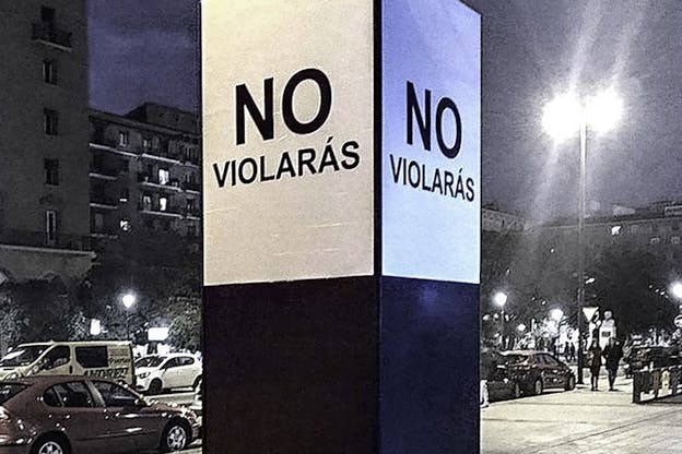 A thick pole in a street surrounded on each side by white posters with the phrase 