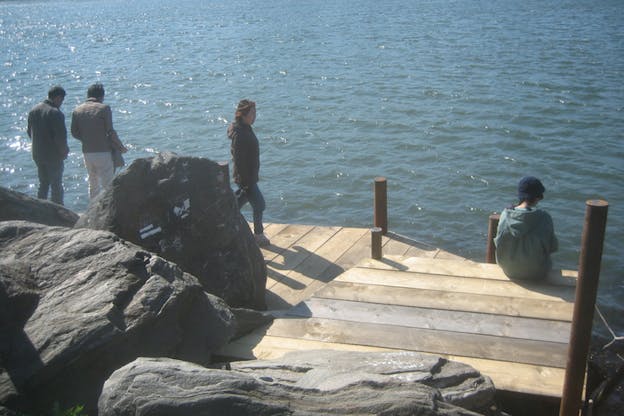 People walking and sitting on a wooden wharf overlooking the water. 