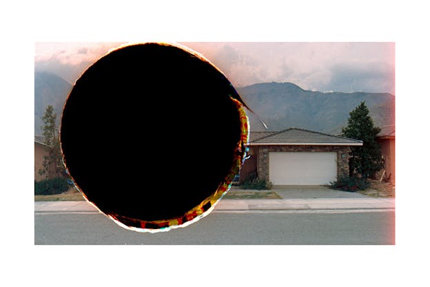 A photograph of a suburban area with a a black cirlce covering the left half of the image.