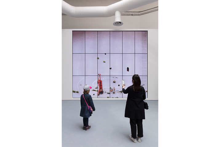 Two figures view a digital illustration the size of a wall. The whole space is white except the illustration which has shapes of red and green.