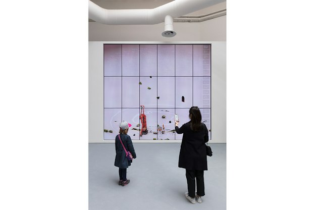 Two figures view a digital illustration the size of a wall. The whole space is white except the illustration which has shapes of red and green.
